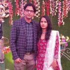 Couple posing under pink cherry blossom tree in white dress and plaid shirt
