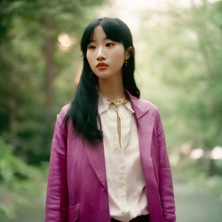 Black-haired woman in purple blazer and white shirt in lush forest setting