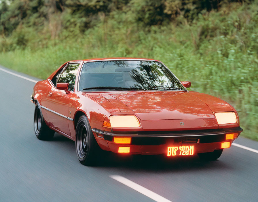 Red Vintage Sports Car Driving on Road Through Lush Greenery