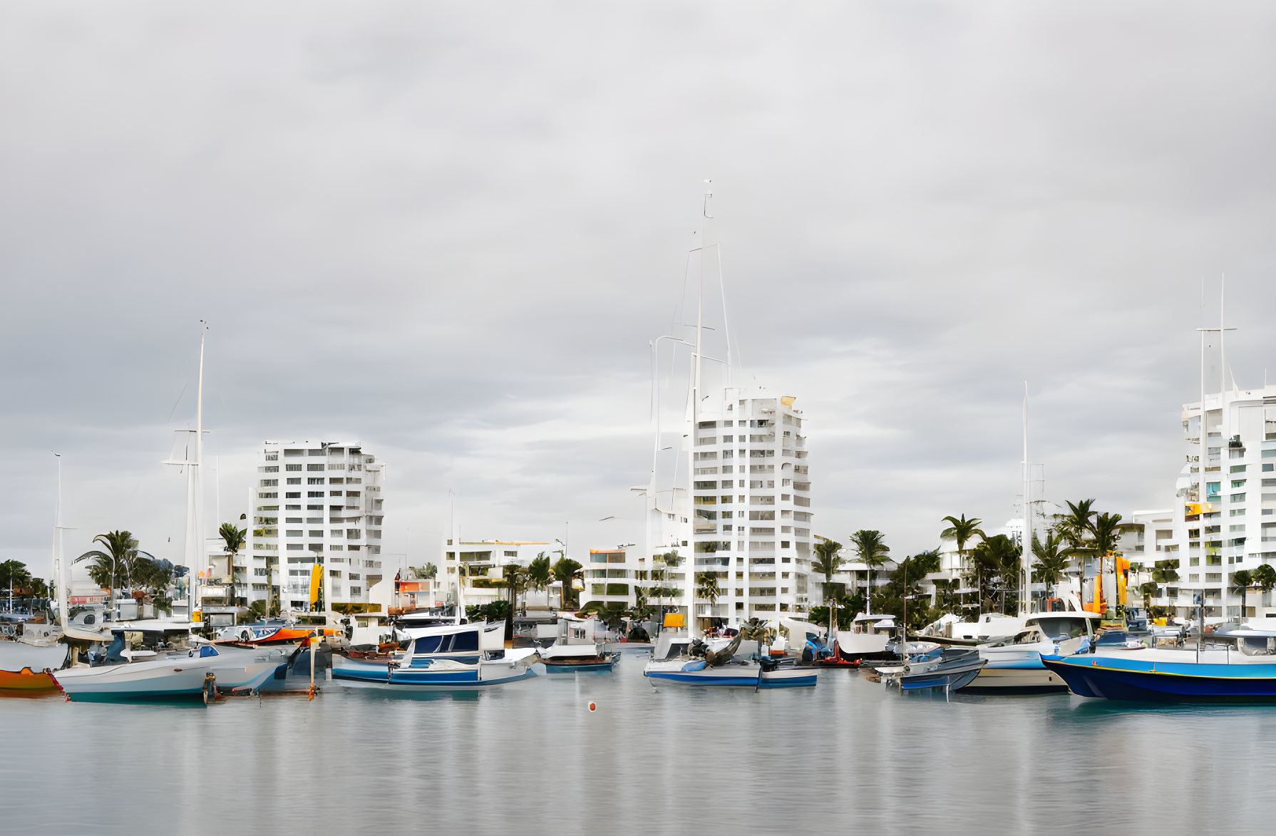 Colorful boats at tranquil marina with modern buildings under overcast sky