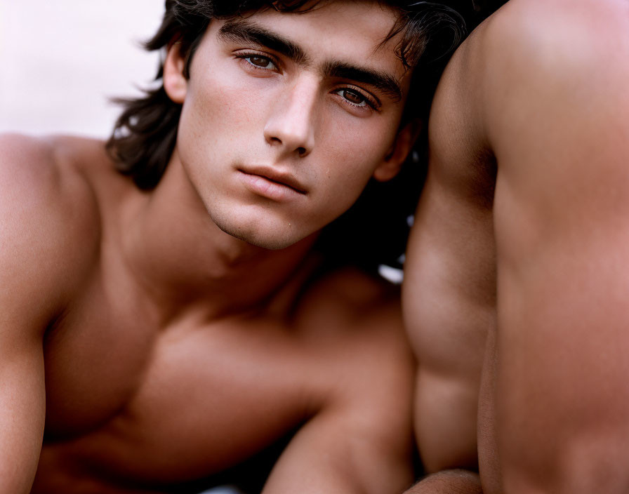 Dark-haired shirtless male gazing thoughtfully.