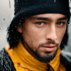 Man in black hat and yellow scarf under umbrella in rain.