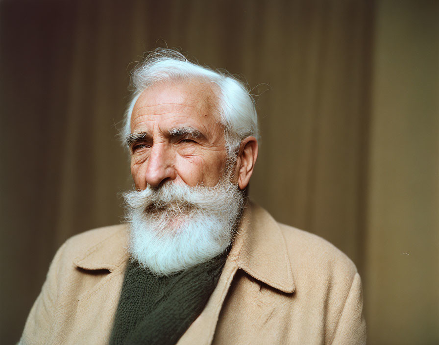 Elderly man in beige coat and green sweater with white beard on tan background