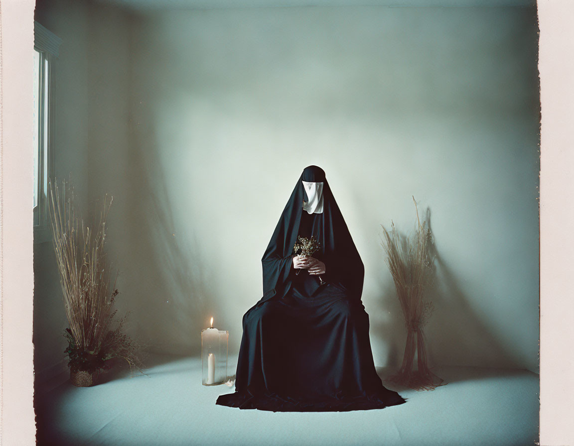 Nun in habit with book, dried plants, and candle on grey backdrop