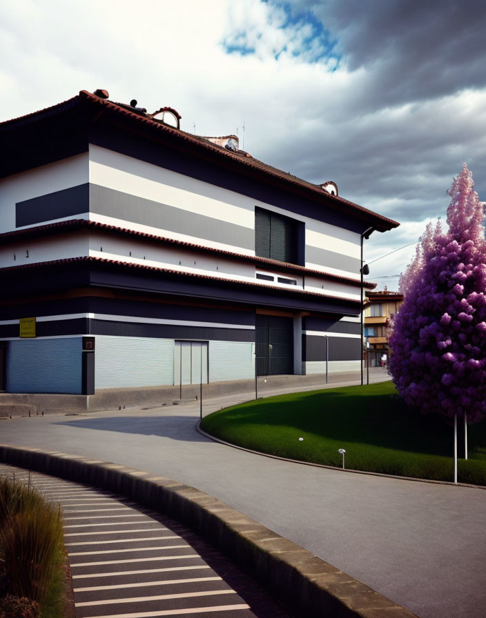 Striped facade modern building next to curved road with purple tree and overcast sky