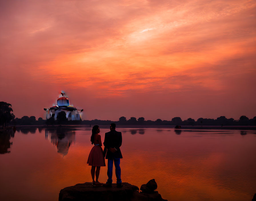 Silhouetted couple by serene lake at sunset with vibrant sky and reflective building.