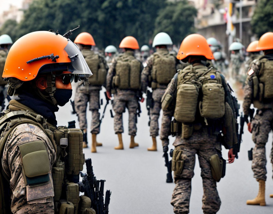 Focused armed soldier with orange visor helmet, surrounded by group of soldiers in background.