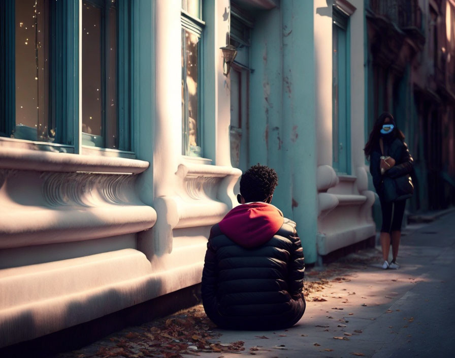 Person in Black and Red Jacket Sitting on City Sidewalk with Masked Figure Passing By on Sunny