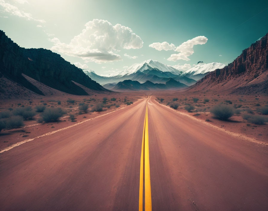 Straight road to snow-capped mountains in desert landscape under bright sky