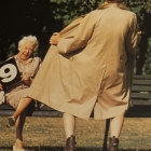 Elderly men chatting on park bench, one with beige blanket