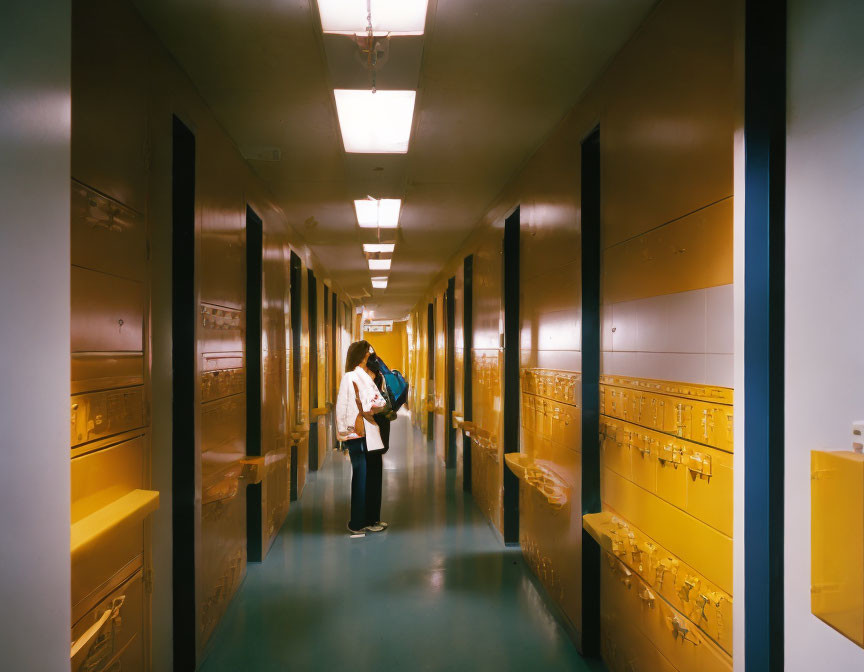 Brightly Lit Corridor with Yellow Lockers and Person Holding Bag