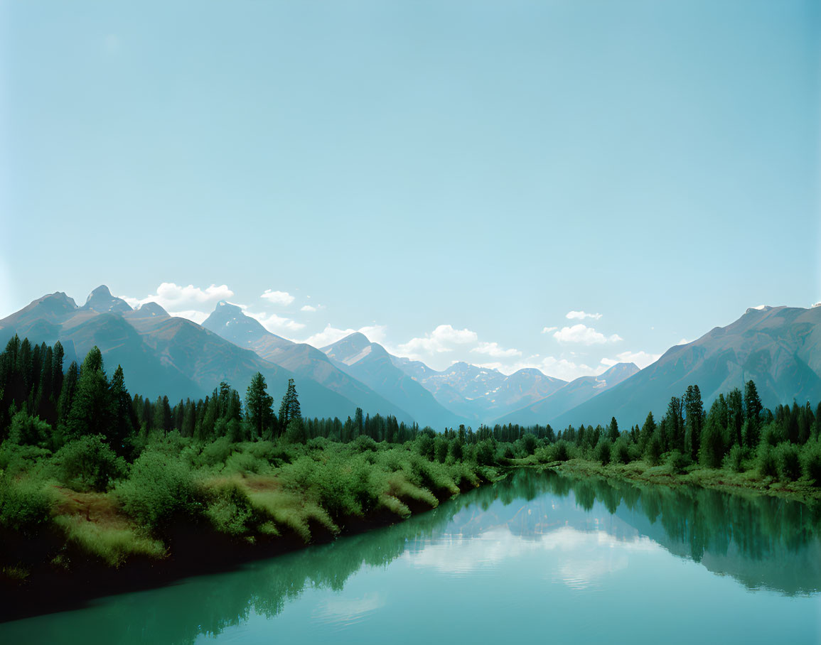 Tranquil river, lush greenery, and majestic mountains under clear sky