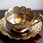 Golden cup and saucer with intricate cut-out patterns on reflective wooden surface