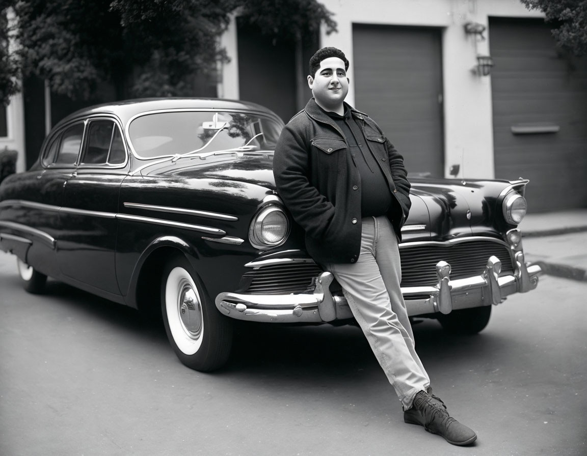 Monochrome image of person by vintage car on residential street