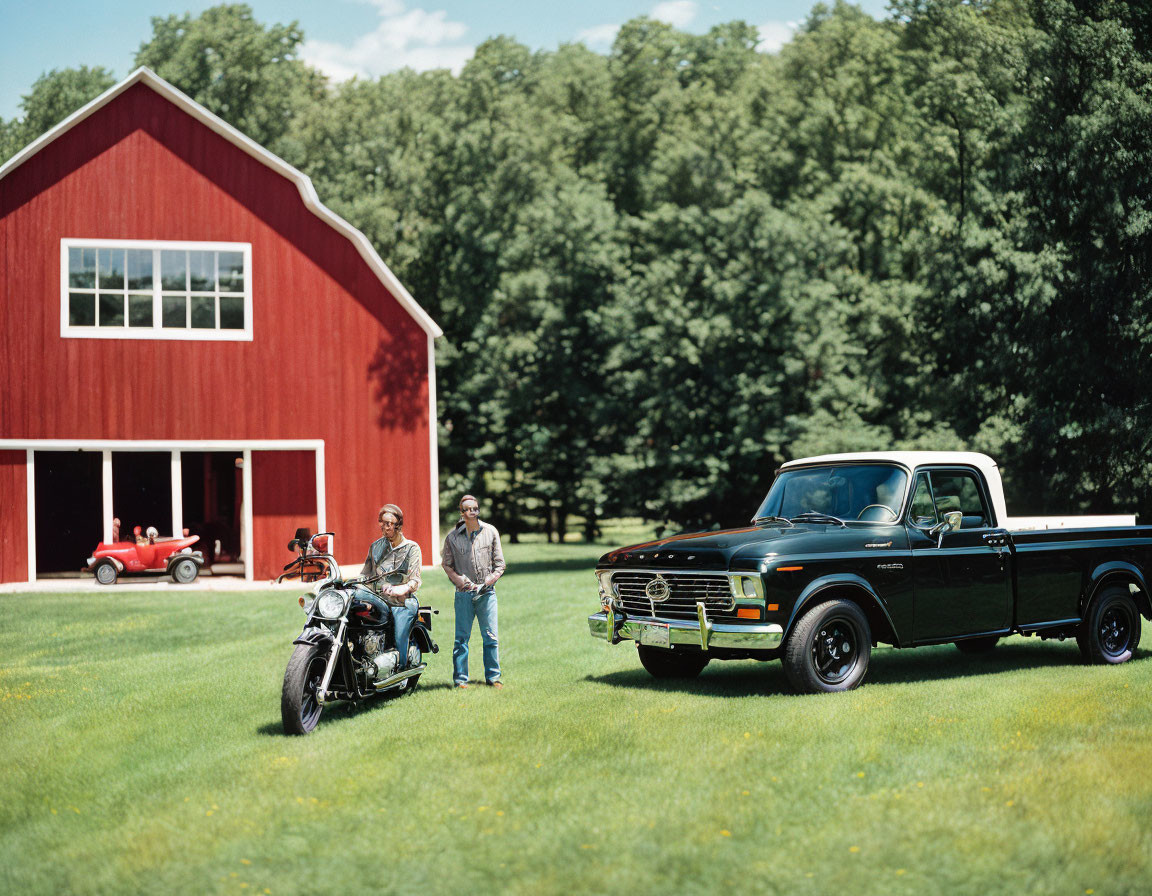 Two people with a motorcycle, black pickup truck, and red barn in a grassy area