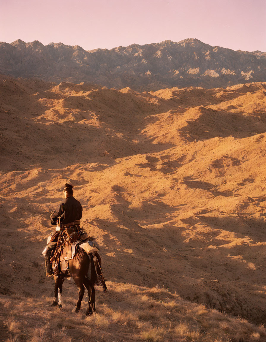 Cowboy riding horse in rugged desert landscape with mountains at golden hour