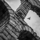 Ancient stone aqueduct with arches and church spires under cloudy sky