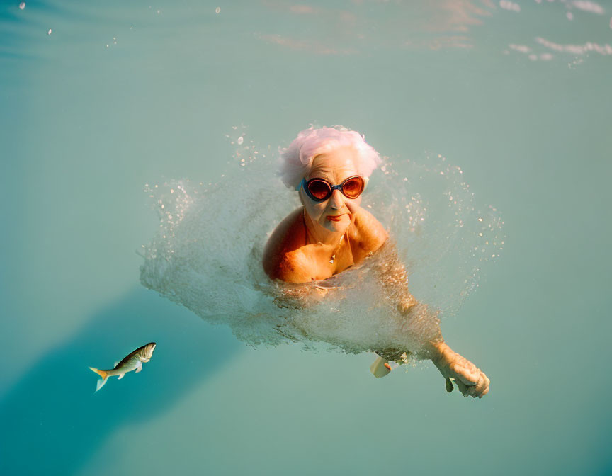 Elderly person with white hair swimming in clear blue water with fish and splash