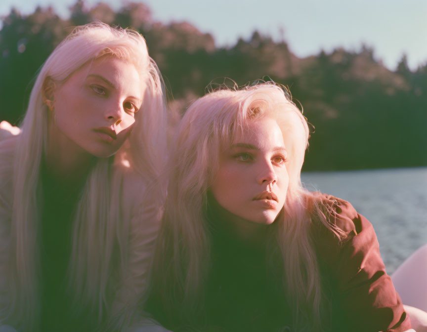 Two women with long blonde hair in white and brown tops outdoors with natural background.