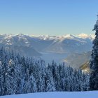 Snowy foreground with volcanic rocks and distant snow-capped volcanoes in a valley under clear blue sky