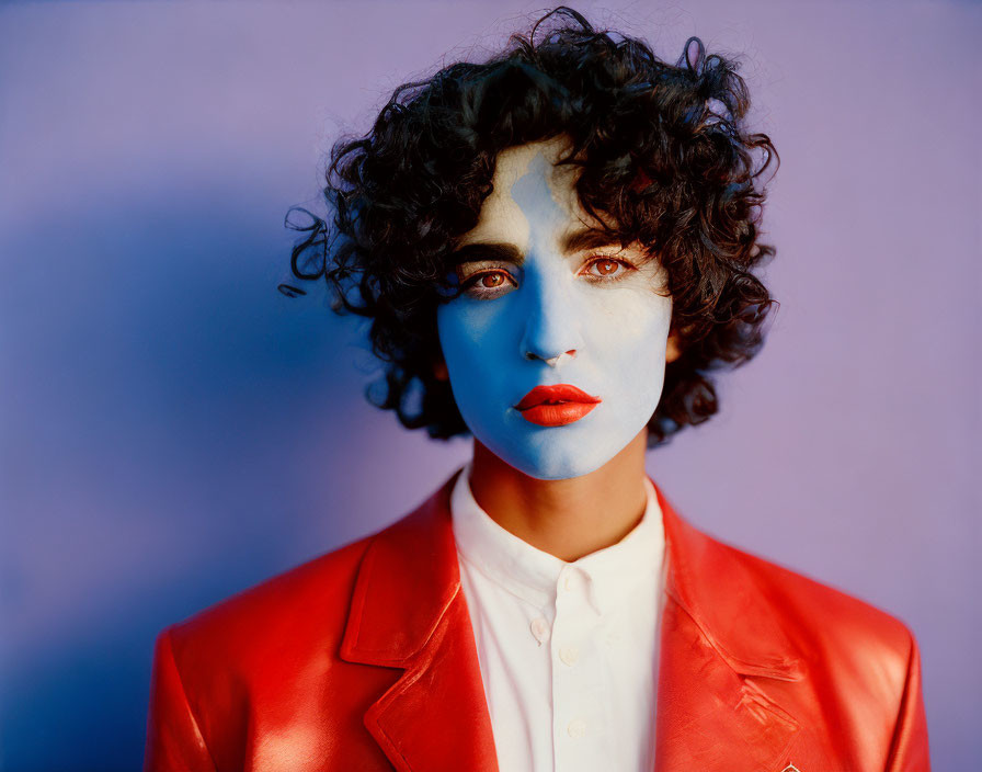 Curly-haired person with blue face paint in red leather jacket on purple background