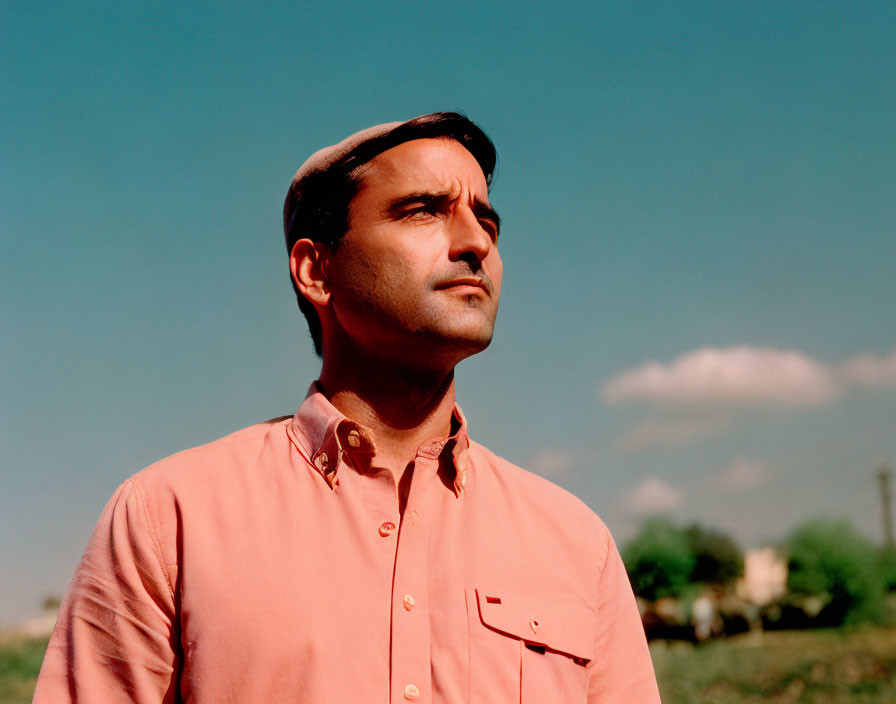 Man in Peach Shirt and Cap Against Blue Sky