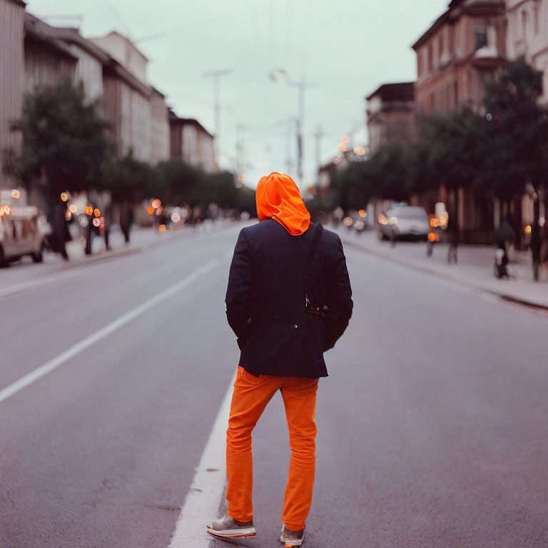 Person in Orange Hoodie Stands in Urban Street at Dusk