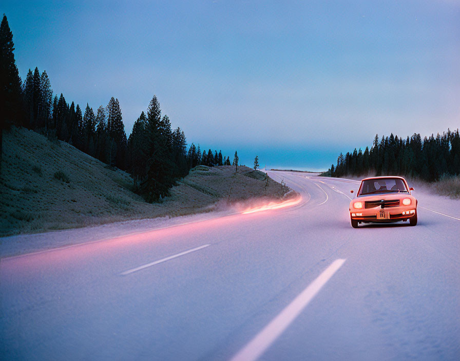 Vintage car drives on snowy road at twilight with light trails, pine trees.