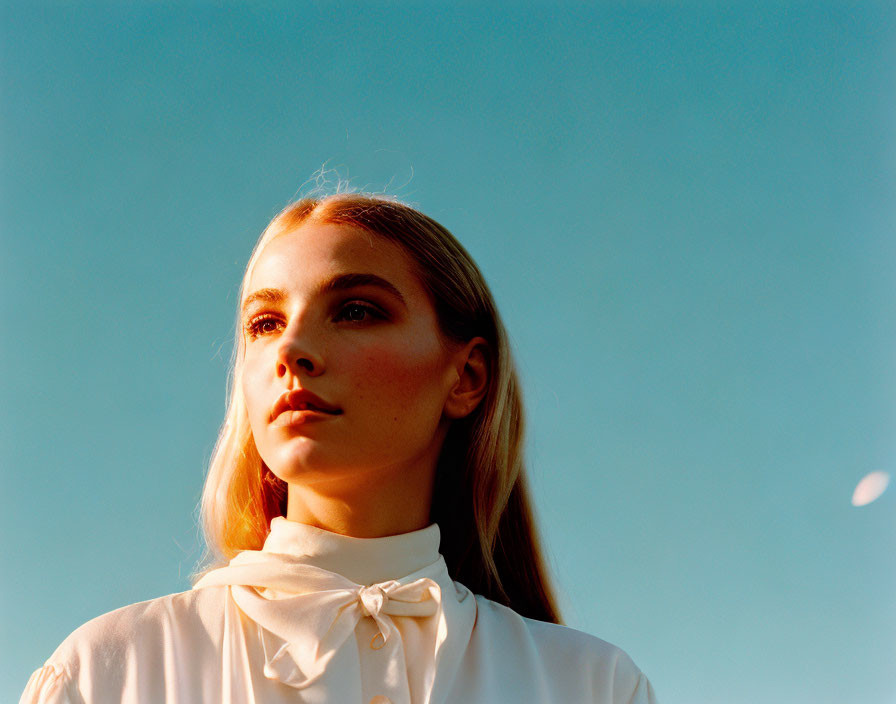 Blonde woman in white blouse gazes under blue sky