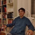 Regal man in ornate attire on throne with bookshelf and luxurious decor