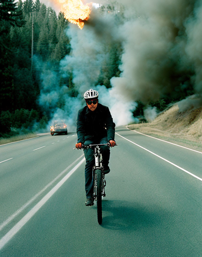 Cyclist in helmet pedals near flaming car on road