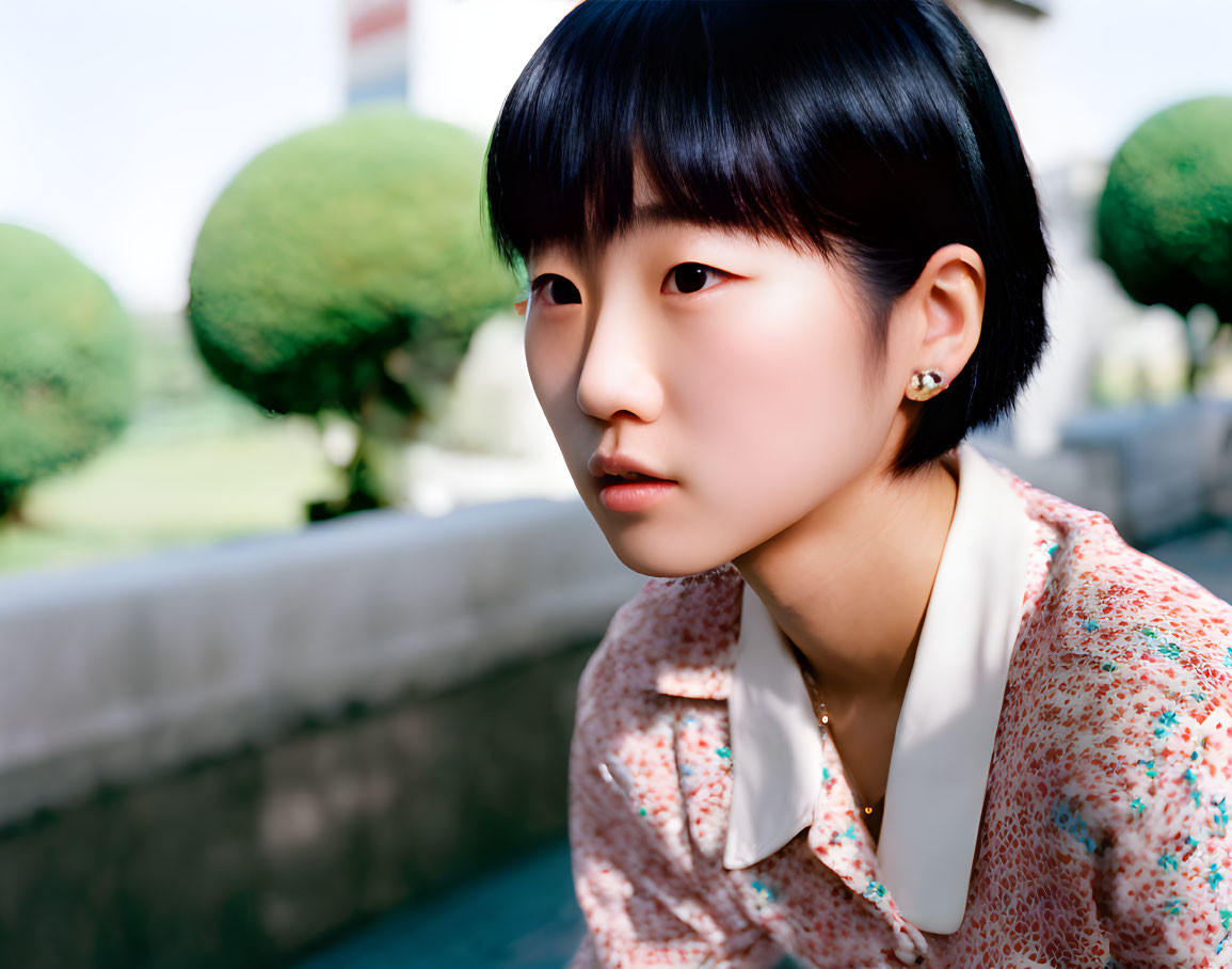 Person with short black hair in floral shirt looking sideways outdoors