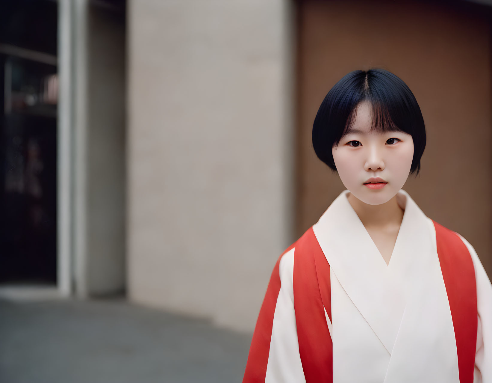 Young individual in traditional white and red outfit with bobbed hair in front of blurred background