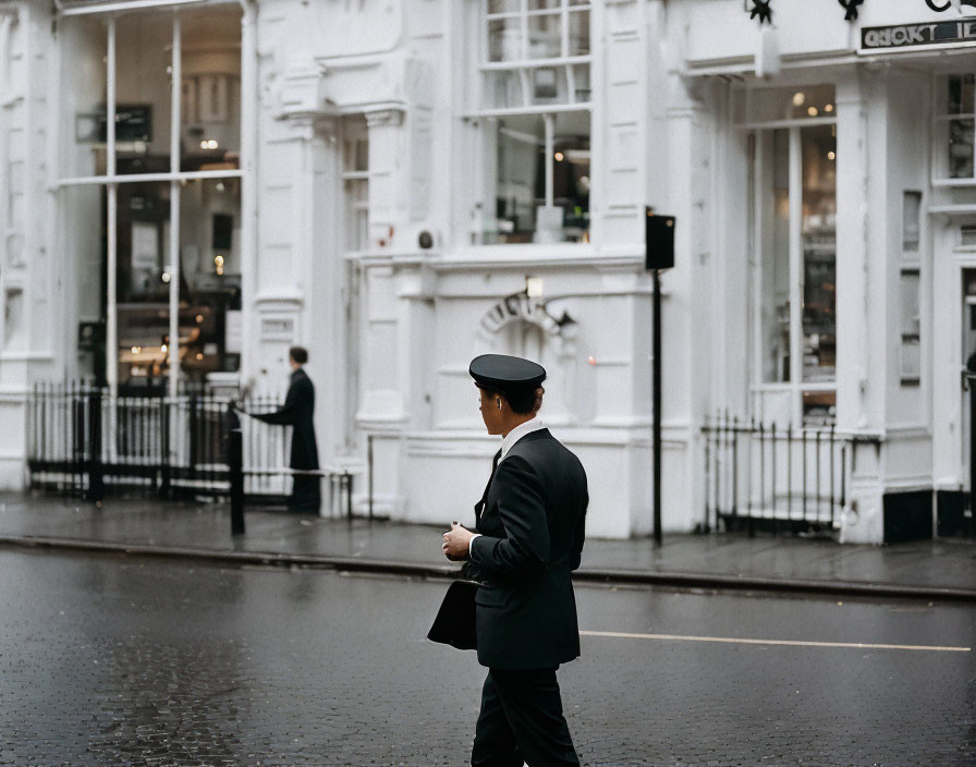 Person in Black Suit and Hat on Wet City Street with White Buildings