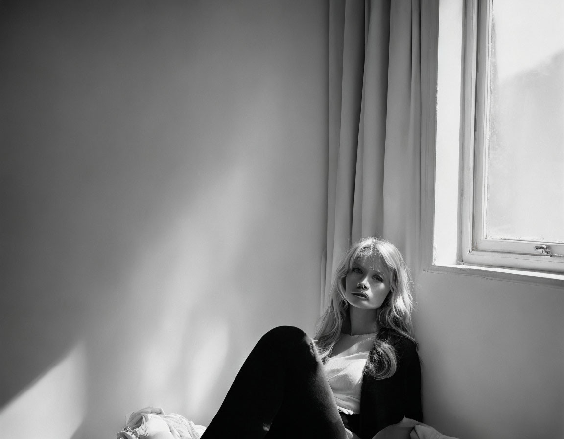 Blonde woman sitting by window in black and white photo