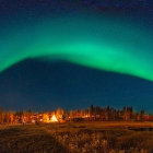 Northern Lights over illuminated forest tents at night