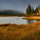 Tranquil autumn lake with mist, golden foliage, tall grass, and cloudy mountains