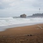 Beach scene with crashing waves, lighthouse, moody sky, and distant figures