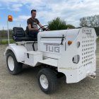 Man in sunglasses drives vintage mini tractor on airfield with airplanes