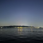 Tranquil lake at twilight with city lights reflection, crescent moon, starry sky, and