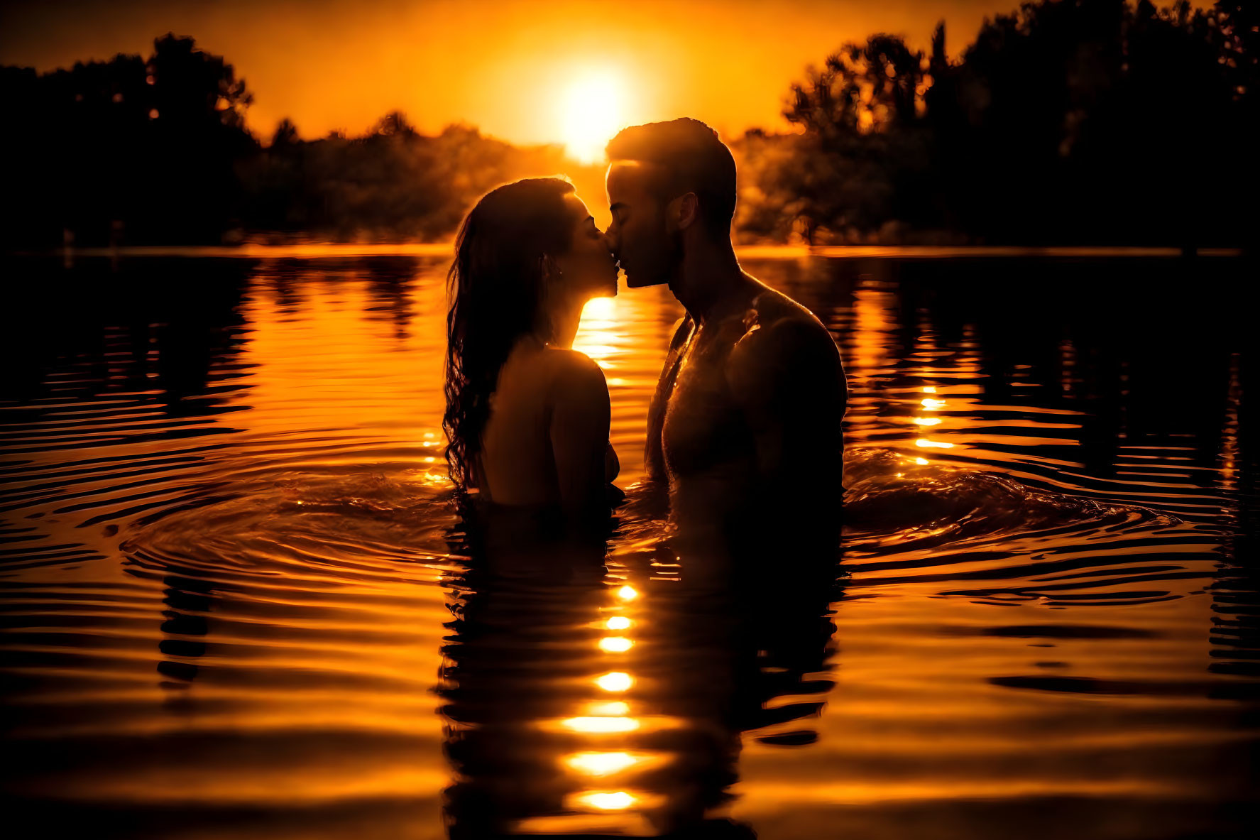 Silhouette of couple in water at sunset with golden glow.