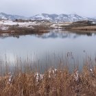 Tranquil landscape with red foliage, reflective lake, snow, and cloudy sky