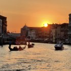 Tranquil waterfront city sunset with sailboat silhouettes, golden sky, and stars.