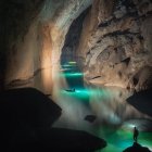 Tranquil fantasy landscape with glowing river, cave, boat, wildlife, and lush vegetation.