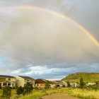 Colorful rainbow over suburban neighborhood with houses and greenery under dramatic sky