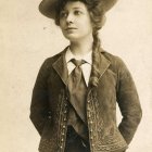 Vintage Woman in Ornate Outfit with Wide-Brimmed Hat and Braid on Creamy Background