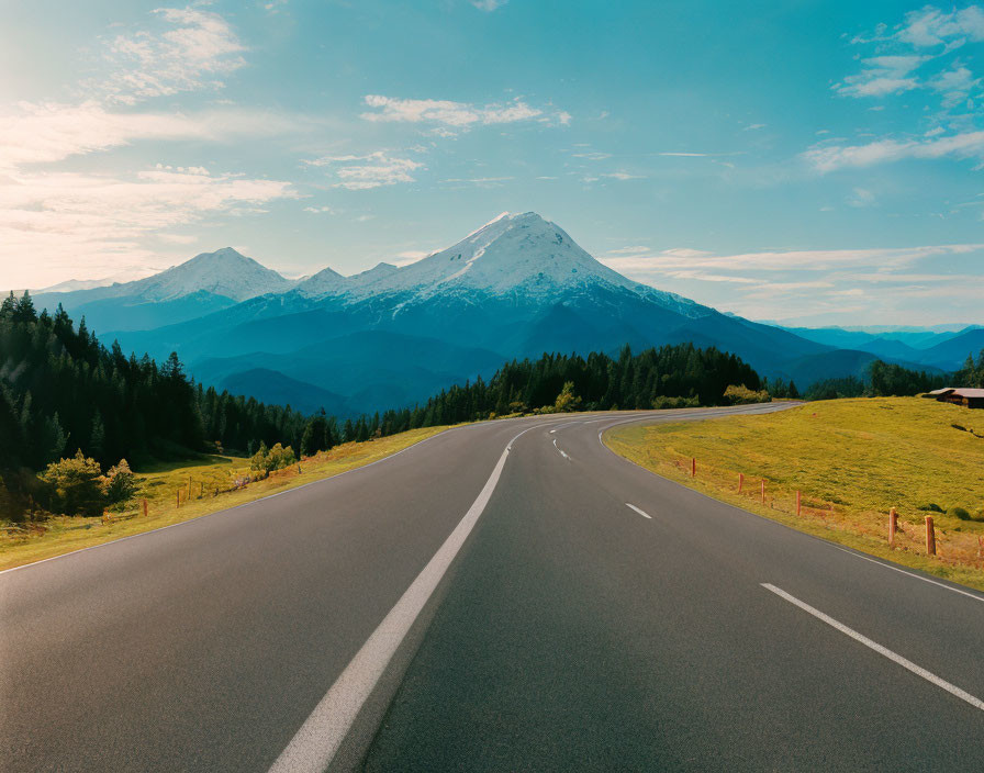 Scenic road with snow-capped mountain, blue sky, and lush greenery