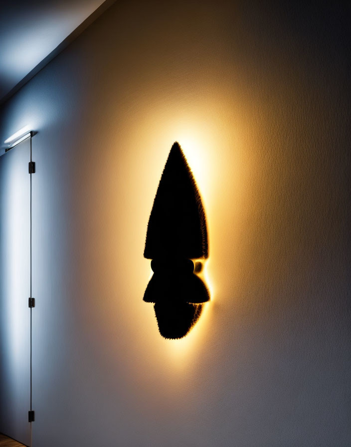 Wall-mounted light casting warm glow creates rocket or surfboard silhouette on beige wall