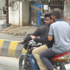 Person in leather jacket on motorcycle with blue headlights in smoky forest.