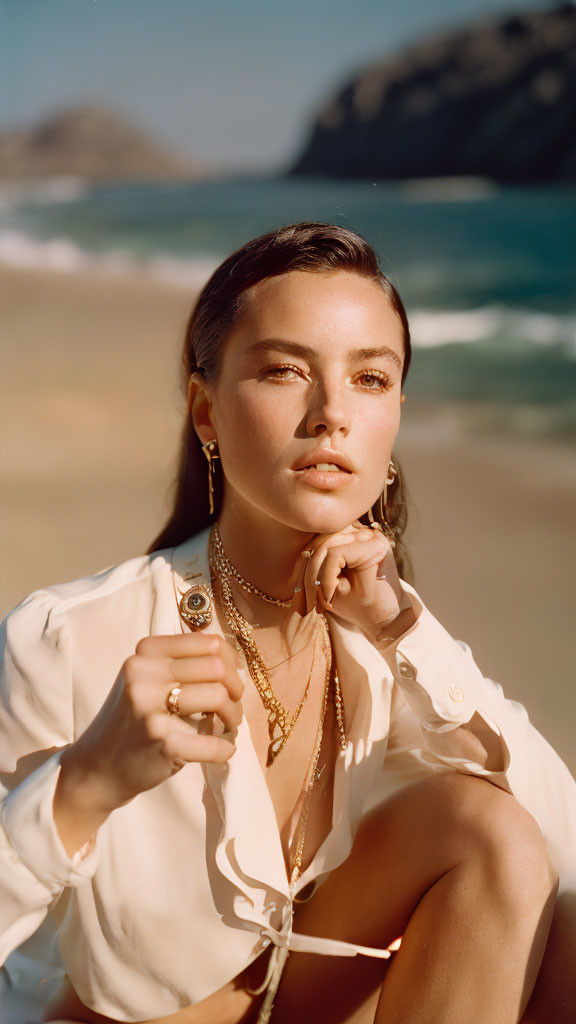 Freckled person in white top on sandy beach with layered necklaces